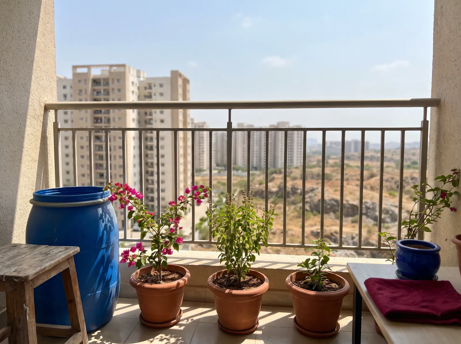 Sunny apartment balcony in Hyderabad with plants and a water drum in summer